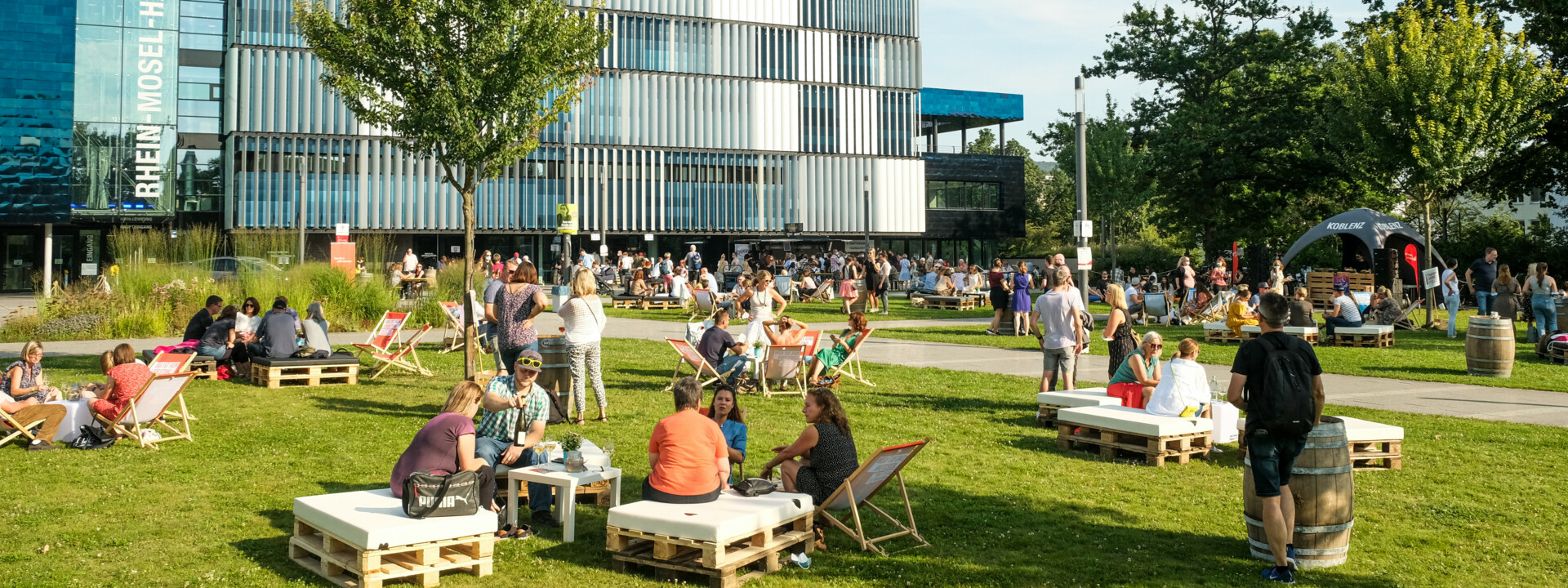 Menschengruppen sitzen verteilt bei der Blaue Stunde vor der Rhein-Mosel-Halle ©Camaze