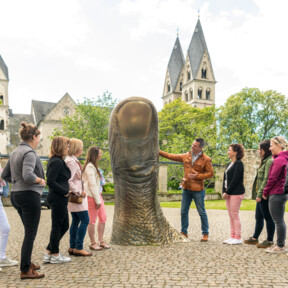 Reisegruppe hört einem Stadtführer zu, während er eine große Daumenstatue vor dem Ludwigmuseum erklärt © Koblenz-Touristik GmbH, Dominik Ketz