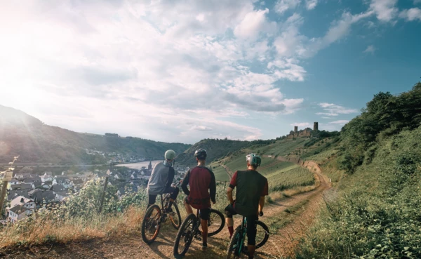 Freundesgruppe auf Mountainbikes auf einem Radweg neben der Mosel mit Burg im Hintergrund