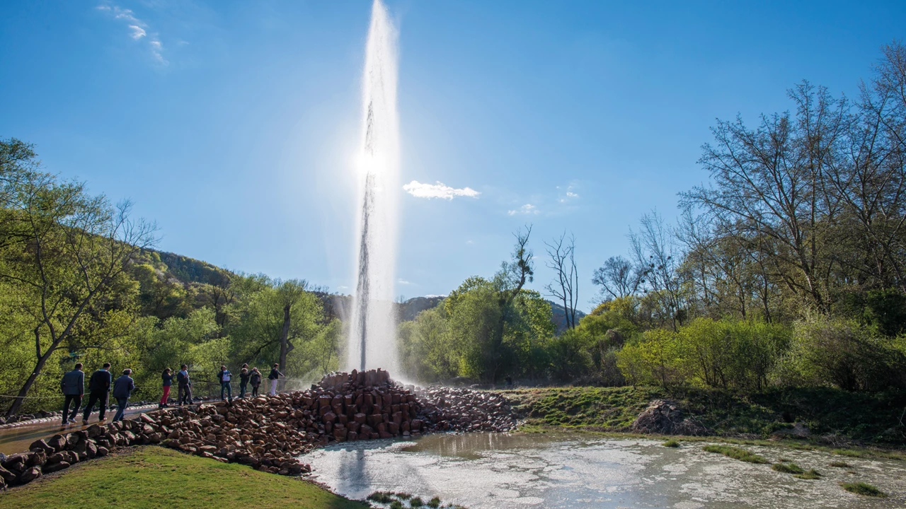 Geysir Andernach hinterbeleuchtet von der Sonne mit beobachtenden Menschen im Vordergrund