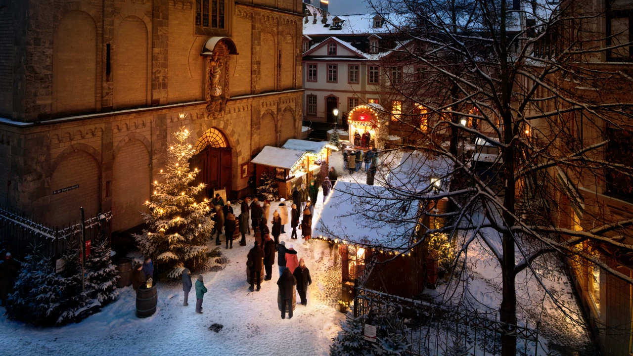Menschen reden, essen und trinken vor beschmuckten und mit Schnee bedeckten Ständen auf dem Vorplatz der Liebfrauenkirche in Koblenz