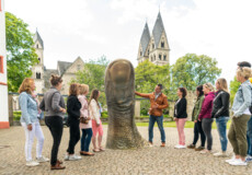 Reisegruppe hört einem Stadtführer zu, während er eine große Daumstatue vor dem Ludwigmuseum erklärt ©Koblenz-Touristik GmbH, Dominik Ketz