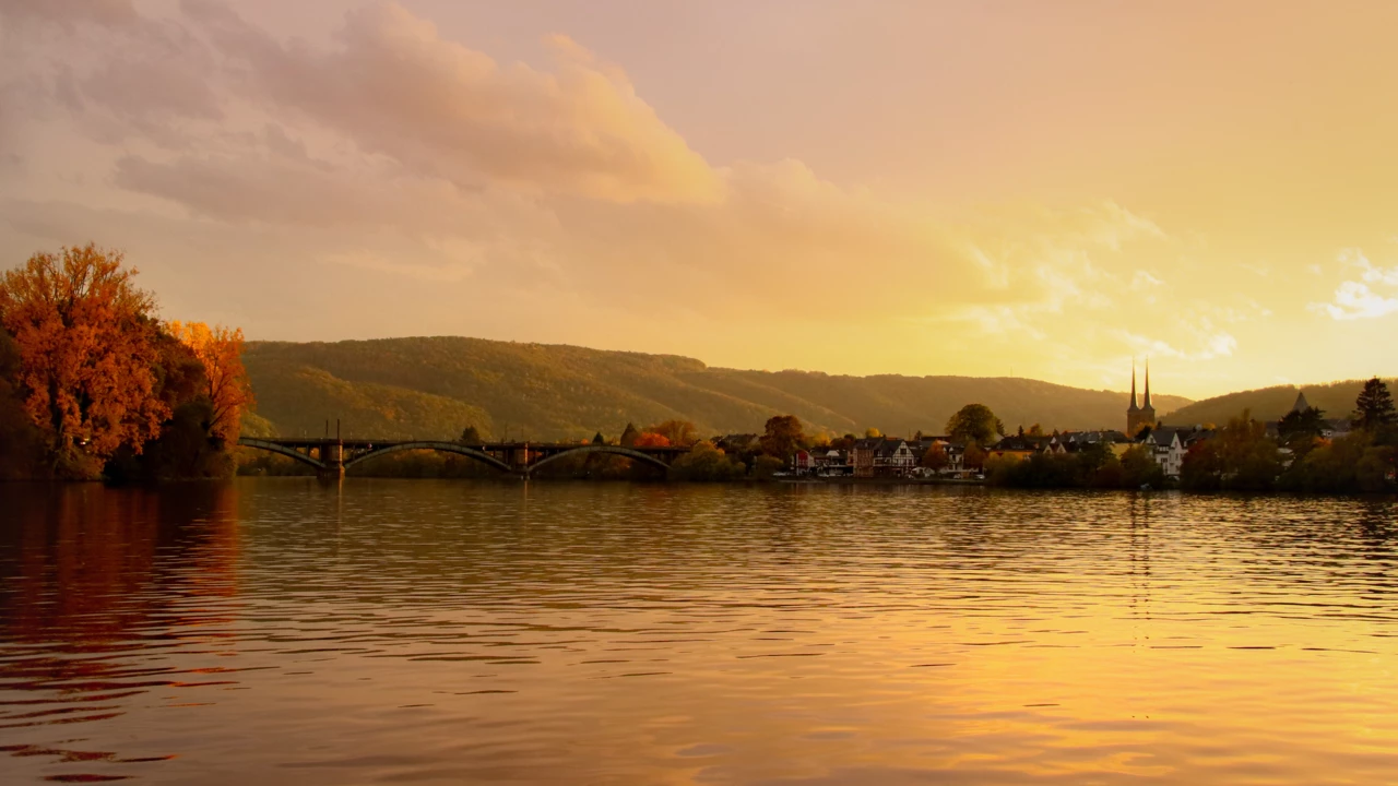 Blick über die Mosel bei Sonnenuntergang, im Hintergrund ein kleiner Ort mit Kirchturmspitze