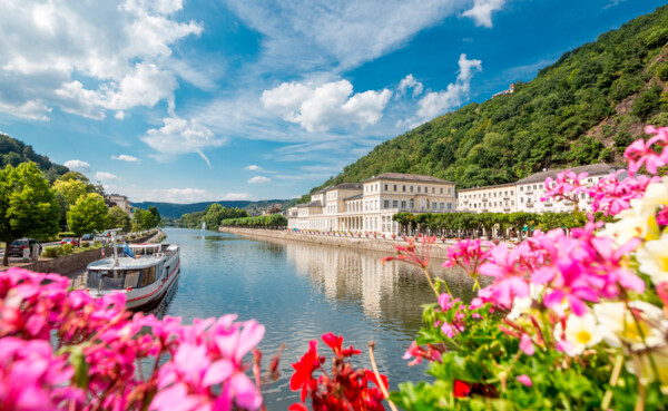 Pinke Blumen bluten vor der Lahn mit romantischen Gebäuden und einem kleinen Schiff im Hintergrund ©