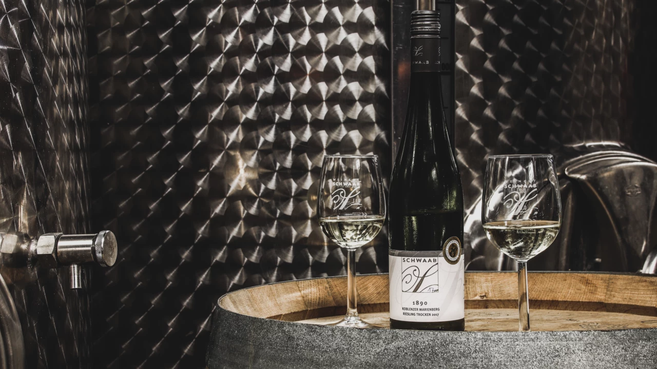 Zwei Weingläser mit Riesling stehen auf einem Fass neben einer Weinflasche