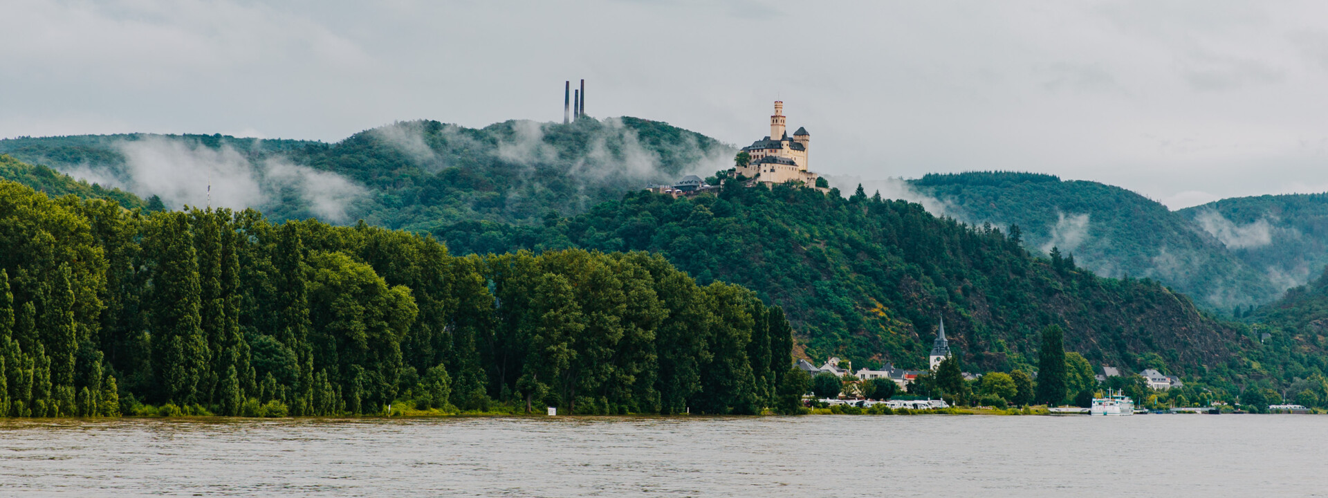 Blick auf die Marksburg vom Rheinufer umgeben von Bergen und Wald mit dem Rhein im Vordergrund ©Koblenz-Touristik GmbH, Henry Tornow