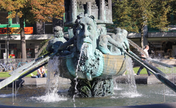 Detaillierte Nahaufnahme der Historiensäule. Der Brunnen ist mit Wasser gefüllt und die frontale Skulptur spritz Wasser aus seinem Mund © 