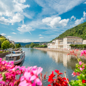 Pinke Blumen bluten vor der Lahn mit romantischen Gebäuden und einem kleinen Schiff im Hintergrund ©