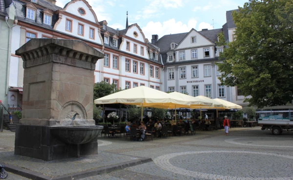 Brunnen auf dem Platz "Am Plan" in Koblenz mit Cafés und erhaltene Altbaugebäuden im Hintergrund