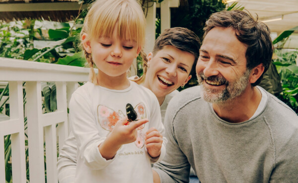 Familie im Schmetterlingsgarten in Sayn lachen während Tochter einen Schmetterling auf ihrem Finger beobachtet © Koblenz-Touristik GmbH, Philip Bruederle