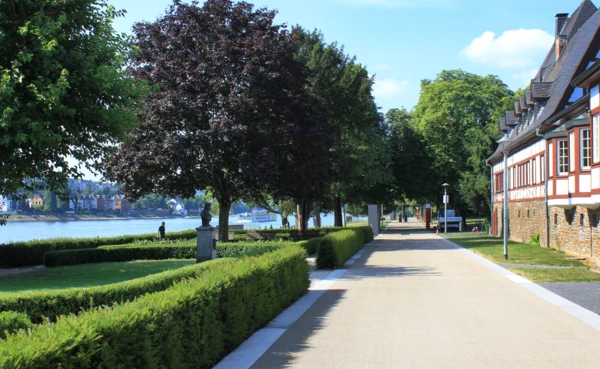 Spazier- und Fahrradweg vor dem Weindorf in den Rheinanlagen umgeben von Statuen, Hecken und Bäumen © Koblenz-Touristik GmbH