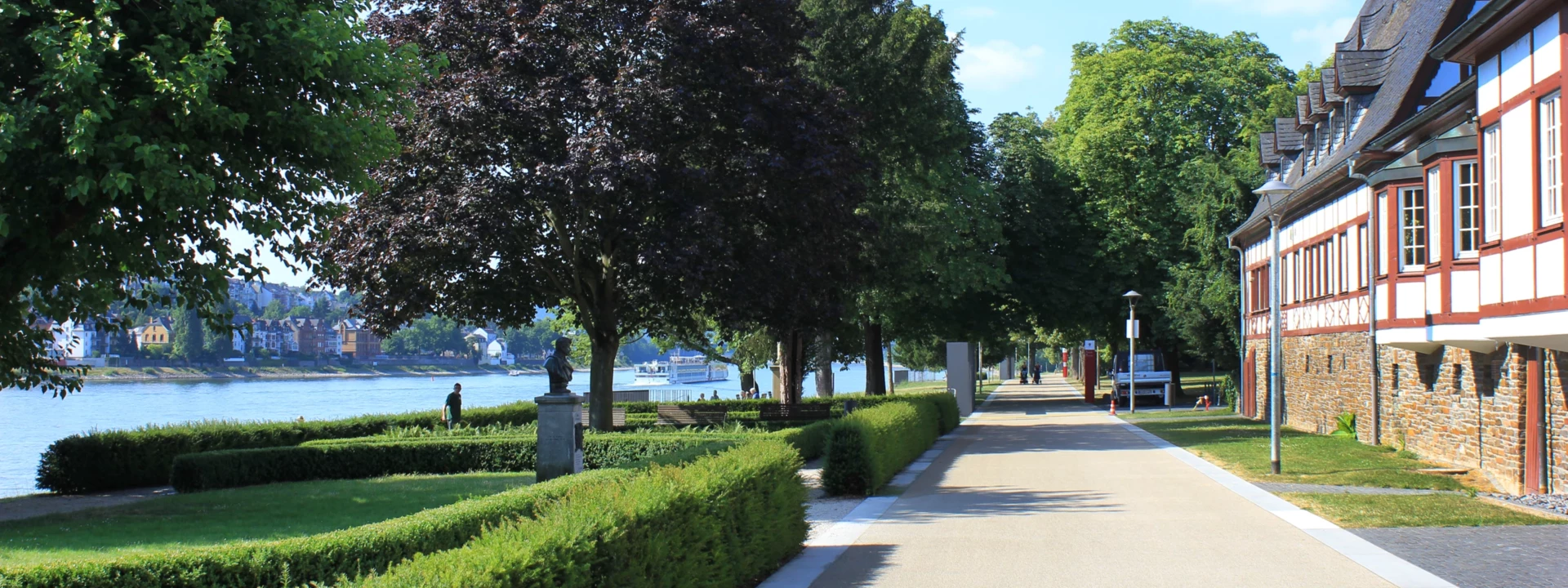 Spazier- und Fahrradweg vor dem Weindorf in den Rheinanlagen umgeben von Statuen, Hecken und Bäumen ©Koblenz-Touristik GmbH