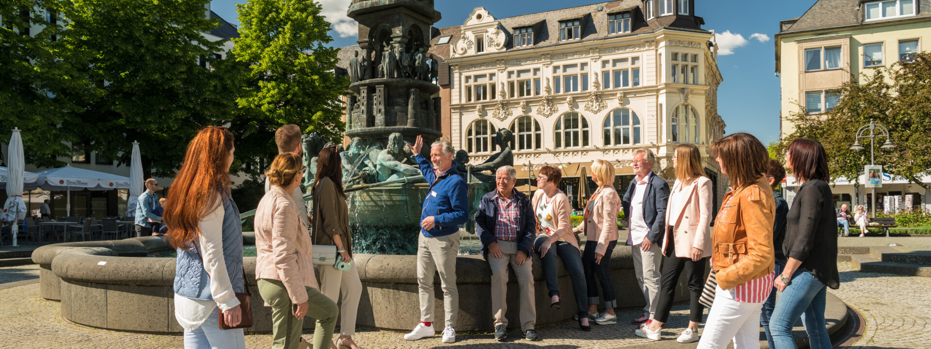 Stadtführung vor Historiensäule am Görresplatz. Menschengruppe hört dem Stadtführer zu. © Stadtführung vor Historiensäule am Görresplatz. Menschengruppe hört dem Stadtführer zu. ©