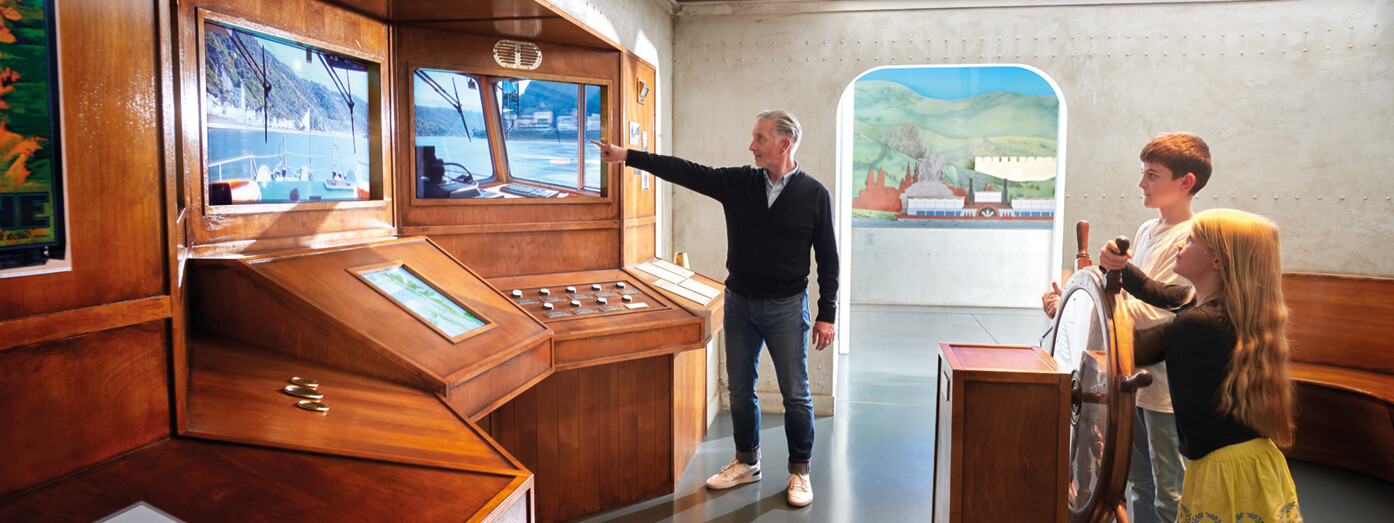Opa zeigt Enkelkinder etwas auf dem Bildschirm in der Schiffsausstellung des Romanticums ©Koblenz-Touristik GmbH, Gauls Opa zeigt Enkelkinder etwas auf dem Bildschirm in der Schiffsausstellung des Romanticums ©Koblenz-Touristik GmbH, Gauls