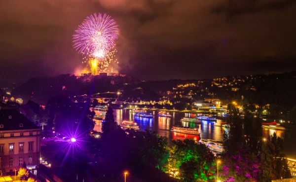 Feuerwerke über der Festung Ehrenbreitstein beleuchten den Nachthimmel. Farblich beleuchtete Schiffe fahren auf dem Rhein.