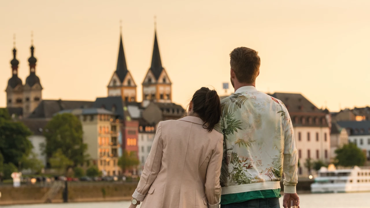 Pärchen mit Wein in der Hand lehnen an einander beim Zuschauen der Stadtsilhouette beim Sonnenuntergang.