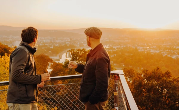 Männer Wein Aussichtsplattform Koblenz Sonnenuntergang © Koblenz-Touristik GmbH, Philip Bruederle Zwei Männer von der Seite halten Weingläser und blicken auf die Stadt Koblenz beim Sonnenuntergang © Koblenz-Touristik GmbH, Philip Bruederle
