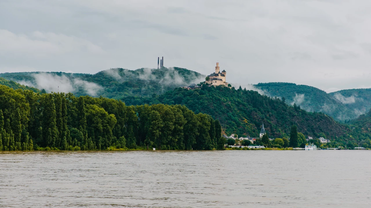 Blick auf die Marksburg vom Rheinufer umgeben von Bergen und Wald mit dem Rhein im Vordergrund