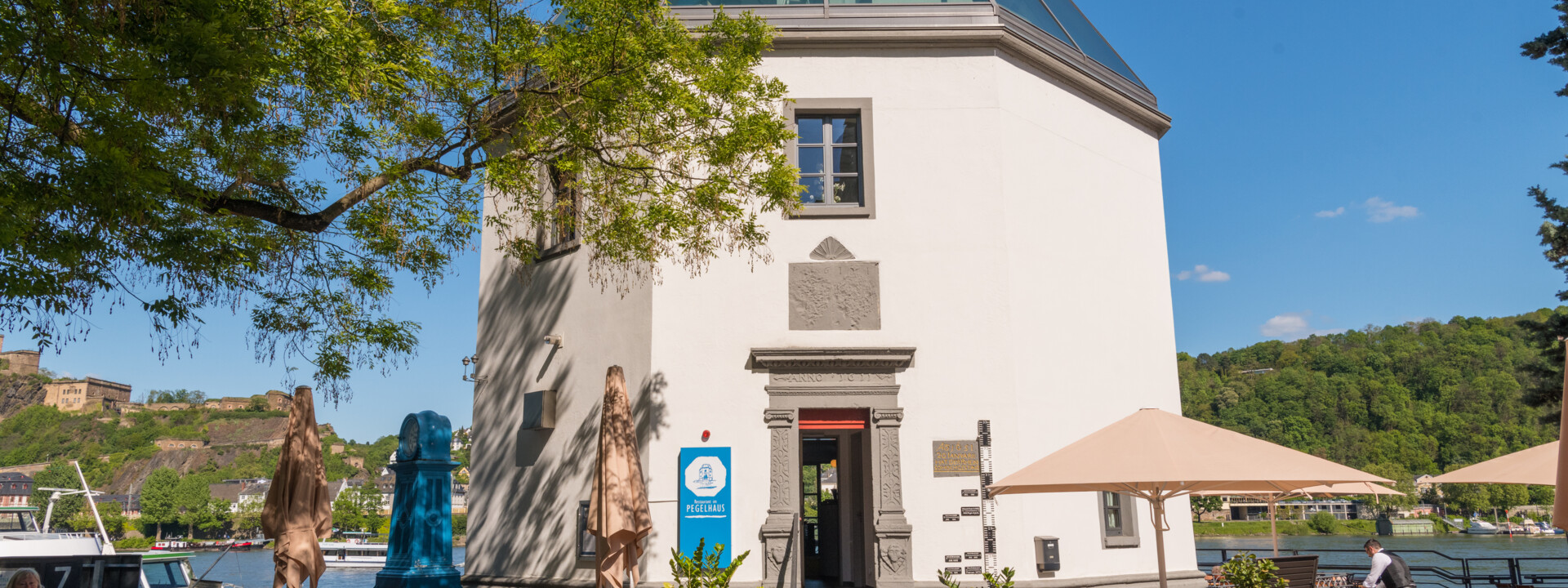 Das Pegelhaus in Koblenz mit Restauranttischen im Vordergrund und dem Rhein und der Festung Ehrenbreitstein im Hintergrund ©Koblenz-Touristik GmbH, Dominik Ketz Das Pegelhaus in Koblenz mit Restauranttischen im Vordergrund und dem Rhein und der Festung Ehrenbreitstein im Hintergrund ©Koblenz-Touristik GmbH, Dominik Ketz
