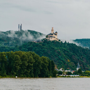 Blick auf die Marksburg vom Rheinufer umgeben von Bergen und Wald mit dem Rhein im Vordergrund © Koblenz-Touristik GmbH, Henry Tornow