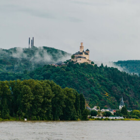 Blick auf die Marksburg vom Rheinufer umgeben von Bergen und Wald mit dem Rhein im Vordergrund ©Koblenz-Touristik GmbH, Henry Tornow