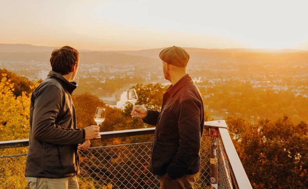 Zwei Männer von der Seite halten Weingläser und blicken auf die Stadt Koblenz beim Sonnenuntergang ©Koblenz-Touristik GmbH, Philip Bruederle
