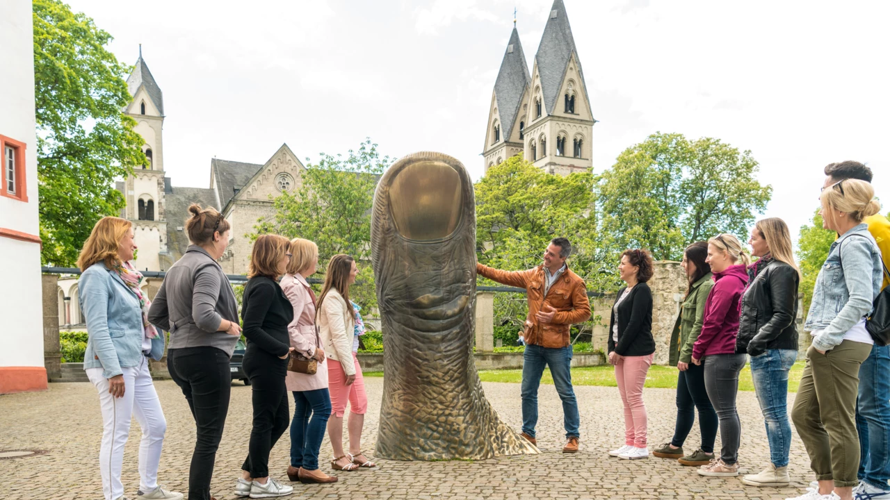 Reisegruppe hört einem Stadtführer zu, während er erklärt eine große Daumstatue vor dem Ludwigmuseum