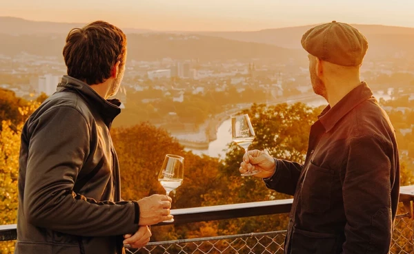 Zwei Männer von der Seite halten Weingläser und blicken auf die Stadt Koblenz beim Sonnenuntergang ©Koblenz-Touristik GmbH, Philip Bruederle