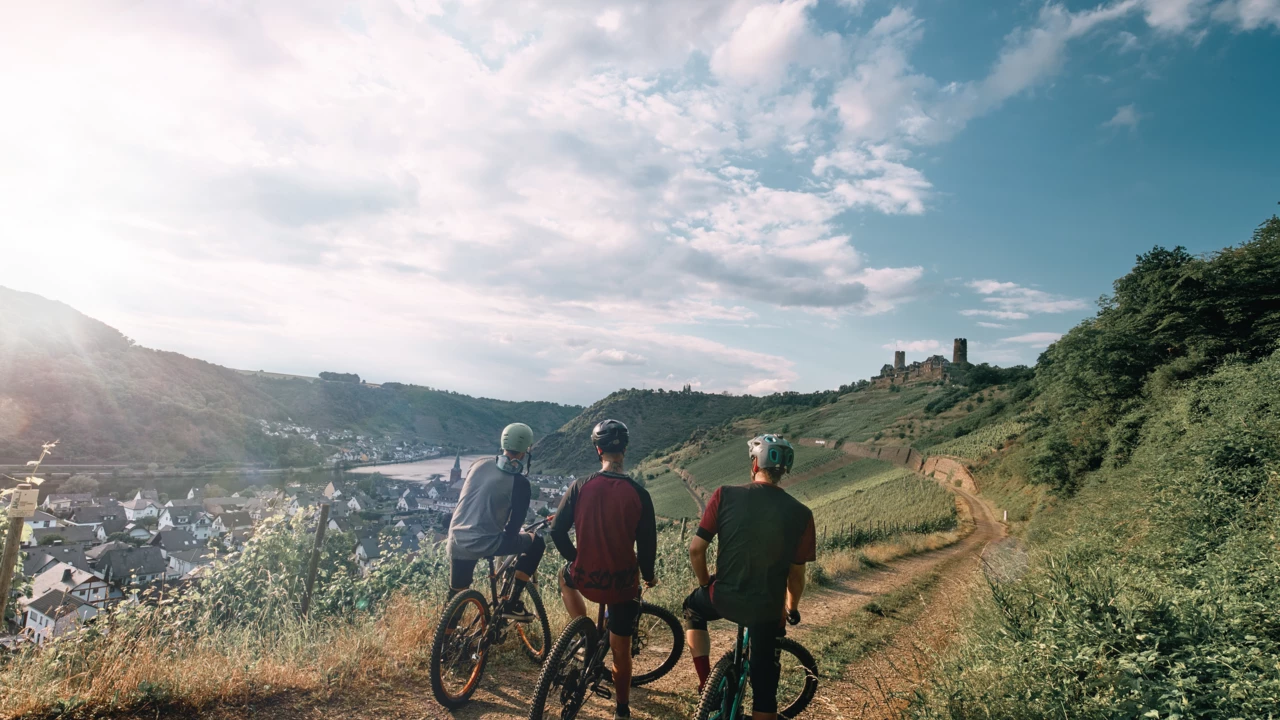 Freundesgruppe auf Mountainbikes auf einem Radweg neben der Mosel mit Burg im Hintergrund