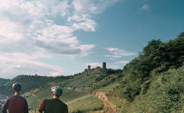 Freundesgruppe auf Mountainbikes auf einem Radweg neben der Mosel mit Burg Thurant im Hintergrund ©Philip Bruederle