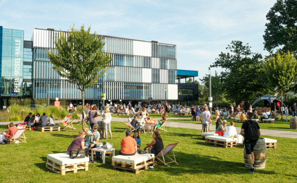 Menschengruppen sitzen verteilt bei der Blaue Stunde vor der Rhein-Mosel-Halle ©Camaze