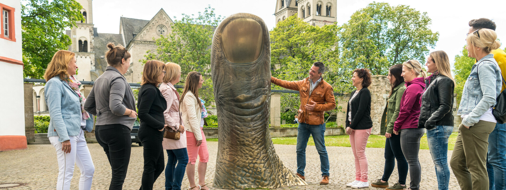 Reisegruppe Stadtführer Daumstatue Basilika St. Kastor Deutschherrenhof Koblenz © Koblenz-Touristik GmbH, Dominik Ketz Reisegruppe hört einem Stadtführer zu, während er eine große Daumenstatue vor dem Ludwigmuseum erklärt © Koblenz-Touristik GmbH, Dominik Ketz