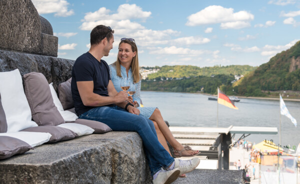 Ein Paar sitzt auf einer Stufe unterhalb des Kaiserdenkmals am Deutschen Eck auf Kissen und trinkt Wein ©Koblenz-Touristik, Dominik Ketz Ein Paar sitzt auf einer Stufe unterhalb des Kaiserdenkmals am Deutschen Eck auf Kissen und trinkt Wein ©Koblenz-Touristik, Dominik Ketz
