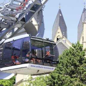 Kabine der Seilbahn Koblenz mit Passagieren. Türme der Basilika St. Kastor im Hintergrund ©Koblenz-Touristik GmbH