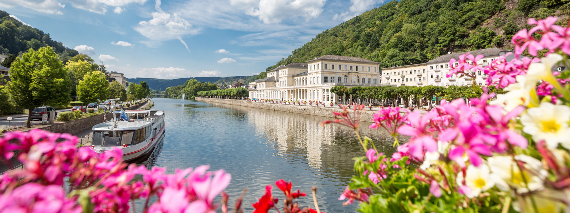 Pinke Blumen bluten vor der Lahn mit romantischen Gebäuden und einem kleinen Schiff im Hintergrund ©