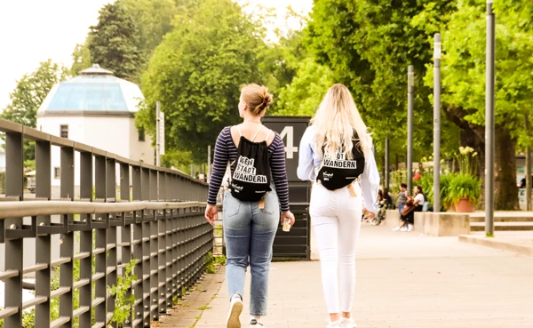 Zwei Mädels sitzen auf einer Mauer mit einer Flasche Wein und schauen ihre WeinStadtWander-Route auf einer Karte an. © Koblenz-Touristik, Johannes Bruchhof