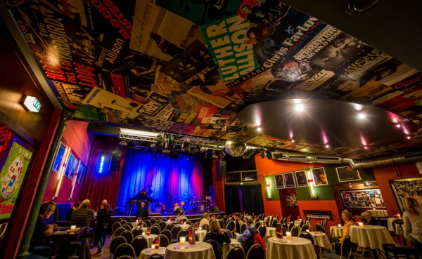 Menschen sitzen an bedeckten Tischen vor einer Bühne in Vorbereitung auf eine Show in Café Hahn