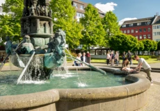 Brunnen "Historiensäule" auf dem Görresplatz in Koblenz umgeben von kleinen Menschengruppen