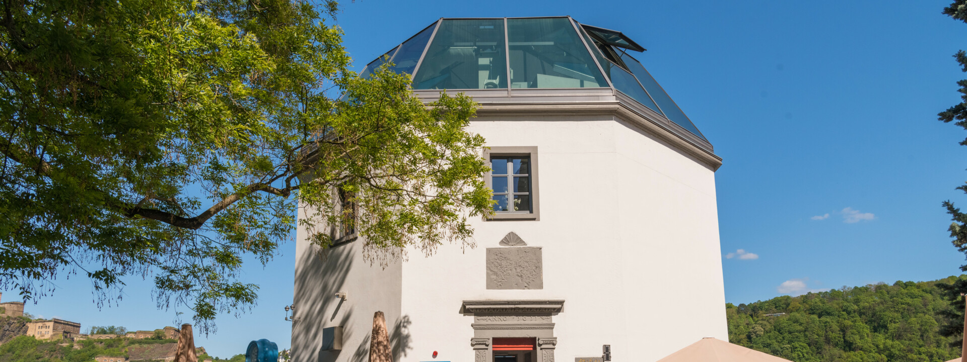 Das Pegelhaus in Koblenz mit Restauranttischen im Vordergrund und dem Rhein und der Festung Ehrenbreitstein im Hintergrund ©Koblenz-Touristik GmbH, Dominik Ketz