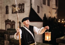 Stadtführer, bekleidet als früherer Nachtwächter, hält Laterne und Hellebarde vor der Alten Burg in Koblenz