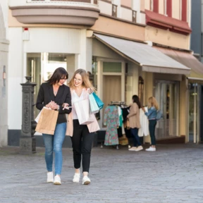 Zwei Frauen mit Einkaufstüten in der Hand schlendern durch eine Gasse in der Altstadt