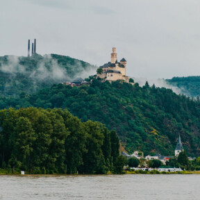 Blick auf die Marksburg vom Rheinufer umgeben von Bergen und Wald mit dem Rhein im Vordergrund ©Koblenz-Touristik GmbH, Henry Tornow