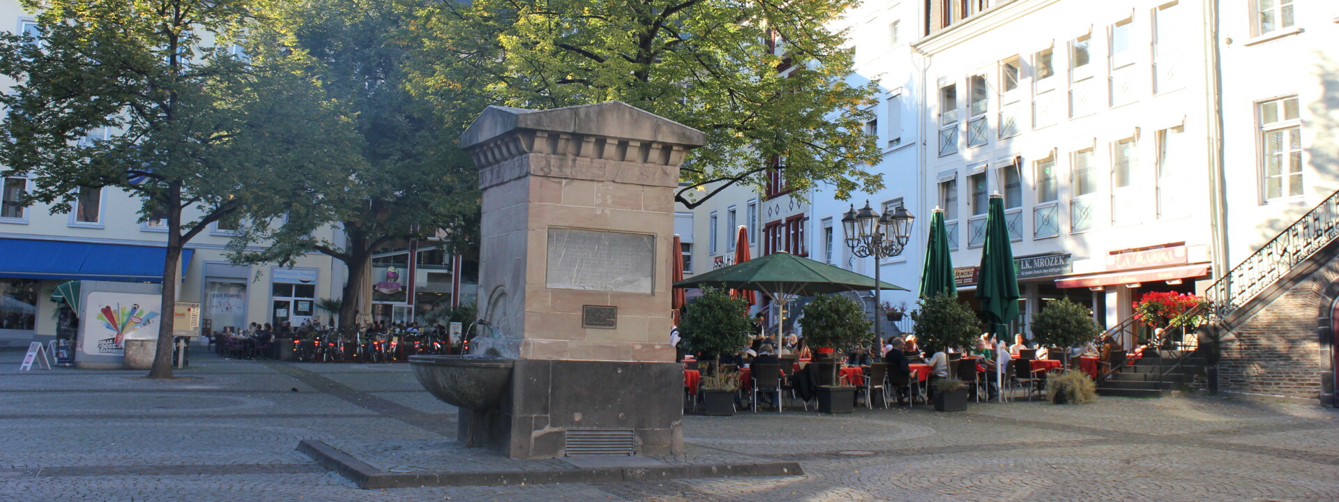 Brunnen auf dem Platz "Am Plan" in Koblenz mit Cafés und Bäumen im Hintergrund ©Koblenz-Touristik GmbH