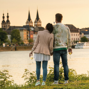 Pärchen mit Wein in der Hand lehnen an einander beim Zuschauen der Stadtsilhouette beim Sonnenuntergang. ©Koblenz-Touristik GmbH, Dominik Ketz