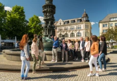 Stadtführung vor Historiensäule am Görresplatz. Menschengruppe hört dem Stadtführer zu.