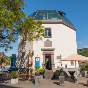 Das Pegelhaus in Koblenz mit Restauranttischen im Vordergrund und dem Rhein und der Festung Ehrenbreitstein im Hintergrund ©Koblenz-Touristik GmbH, Dominik Ketz