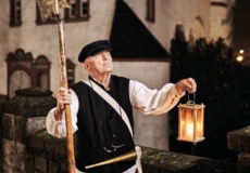 Stadtführer, bekleidet als früherer Nachtwächter, hält Laterne und Hellebarde vor der Alten Burg in Koblenz