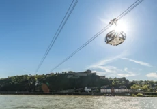 Die Seilbahn Koblenz hinterbeleuchtet von der Sonne mit Rhein im Vordergrund und Festung Ehrenbreitstein im Hintergrund