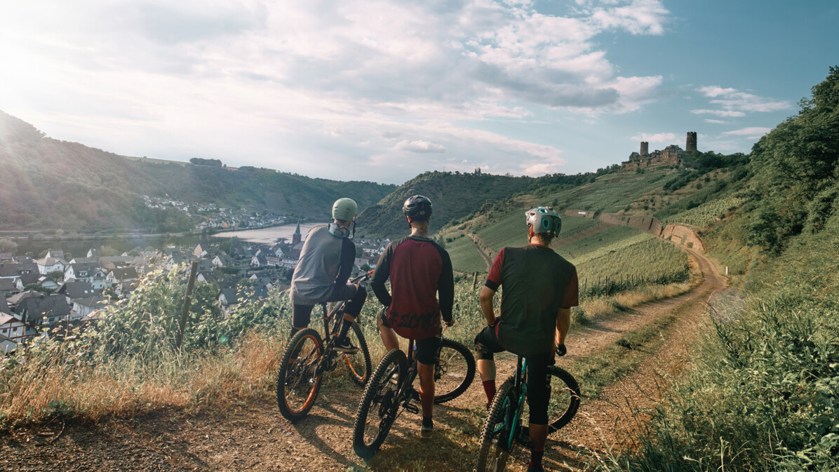 © Philip Bruederle Freundesgruppe auf Mountainbikes auf einem Radweg neben der Mosel mit Burg Thurant im Hintergrund © Philip Bruederle