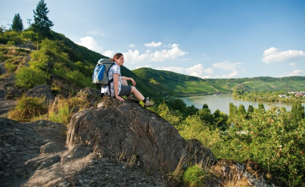 Frau sitzt auf einem Stein über dem Rhein auf dem RheinBurgenWeg Wanderweg